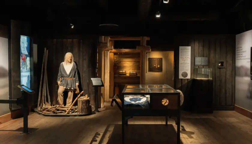 Vikingamuseum Stockholm: en vaxdocka av en viking med yxa, utställningsmontrar med föremål och informationstavlor.