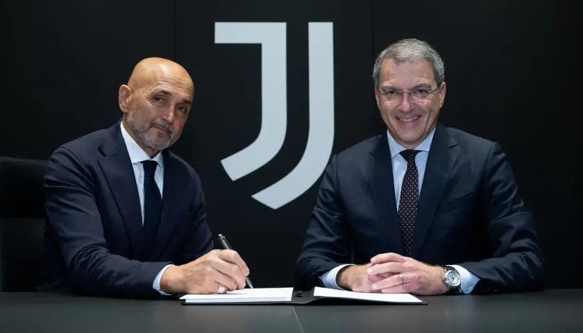 Dwóch mężczyzn w garniturach, prawdopodobnie trenerzy Juventusu, siedzi przy stole. Jeden z nich podpisuje dokumenty.