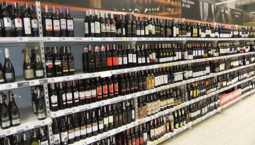 Rzędy butelek wina, w tym wino z suszonych winogron, na półkach sklepowych.