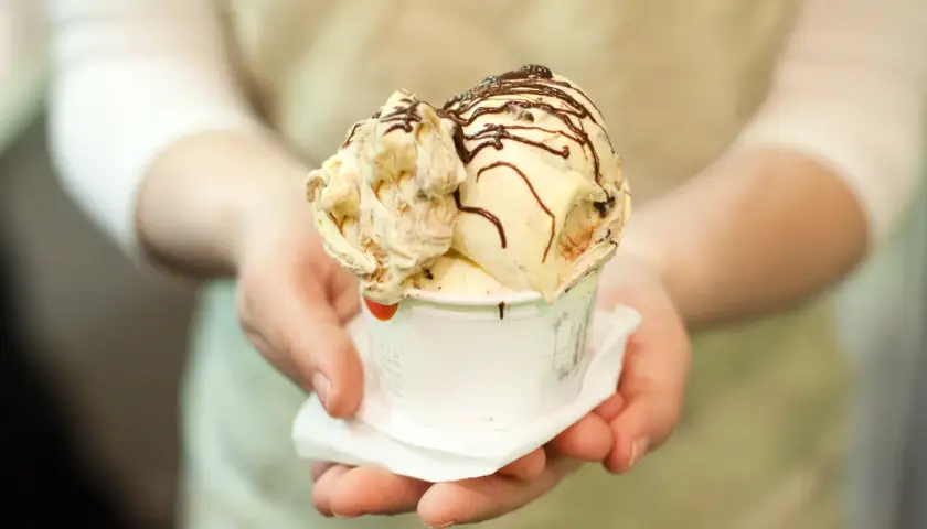 Un cono di gelato artigianale, con variegature e scaglie di cioccolato, pronto per essere gustato, un assaggio della storia del gelato.