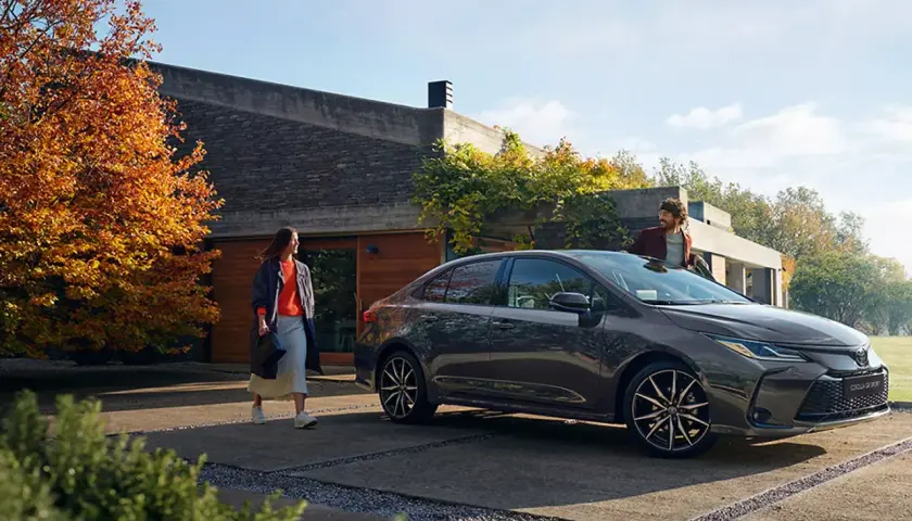 Un hombre y una mujer junto a un Toyota Corolla oscuro frente a una casa moderna.