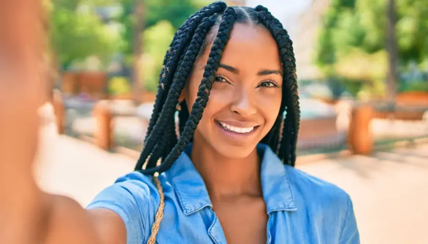 Sonrisa radiante de una mujer con distintos tipos de trenzas africanas, luciendo un estilo moderno y seguro.