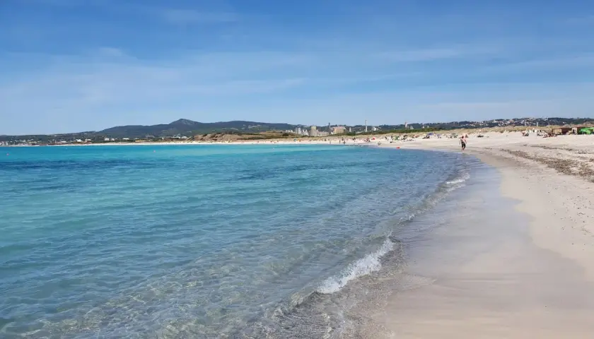 Plage de sable fin à Vada, eaux turquoise, ciel bleu, quelques personnes profitent du soleil.