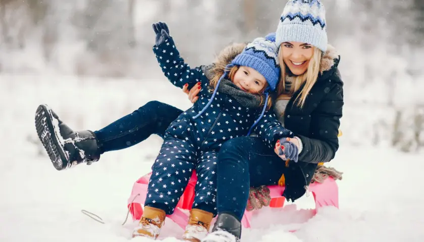 Radosne ferie zimowe 2026 lubelskie! Mama i córka na sankach, śmieją się w śnieżnym krajobrazie.