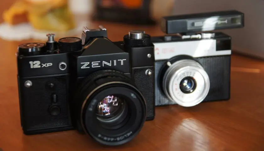 Dwa klasyczne aparaty na film: czarny Zenit 12XP i srebrno-czarny Smiena z lampą błyskową.
