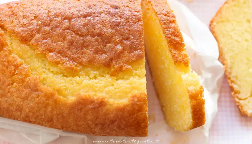 Un soffice plumcake allo yogurt, dorato e invitante, tagliato a fette su carta bianca.
