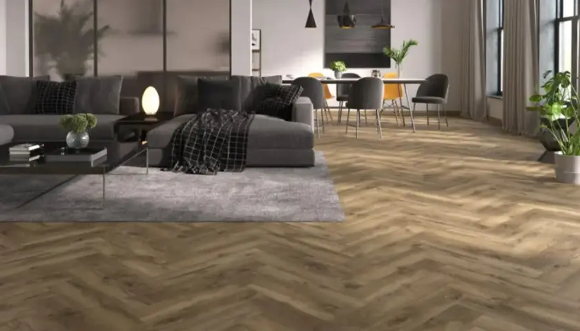 Drewniana podłoga w jodełkę w odcieniu wenge, tworząca ciepłą atmosferę w nowoczesnym salonie z szarą sofą i jadalnią.