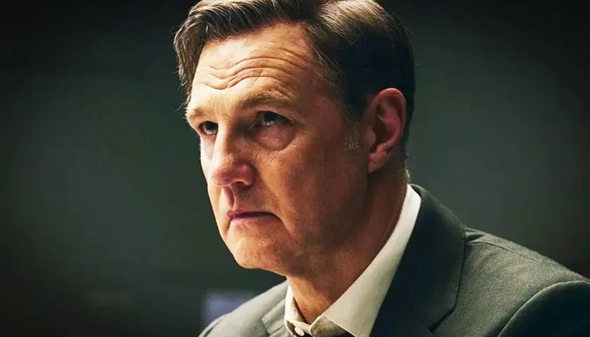 En man i kostym med rynkad panna, kanske en karaktär från nya brittiska serier.