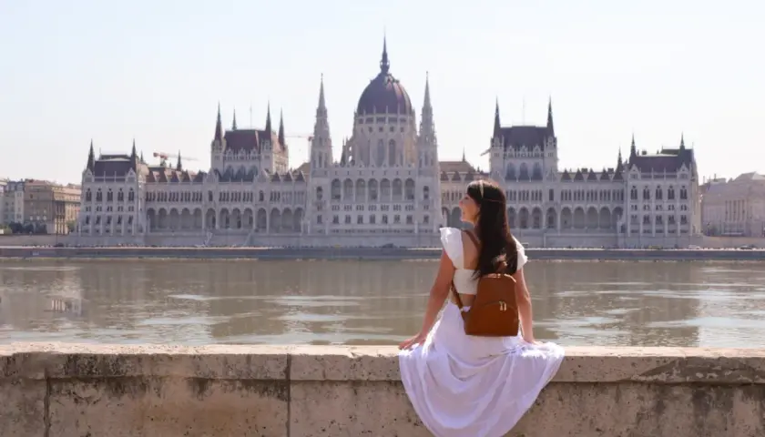 Mujer con mochila admira el Parlamento de Budapest, un lugar imprescindible que ver en Budapest.