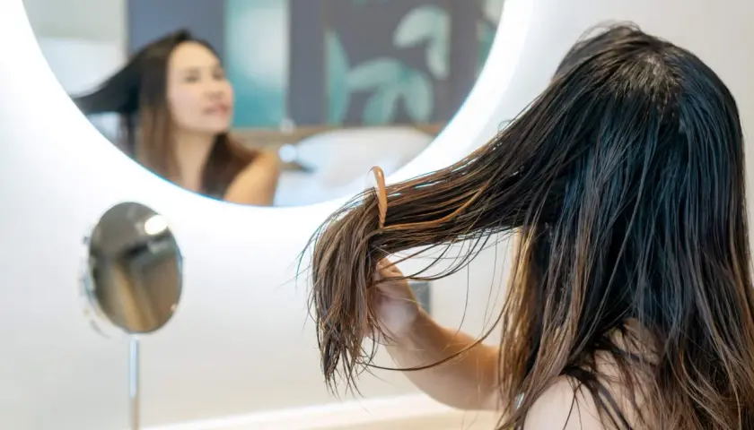 Una joven se peina el pelo mojado frente a un espejo. El pelo adolescentes, largo y castaño, cae en mechones.