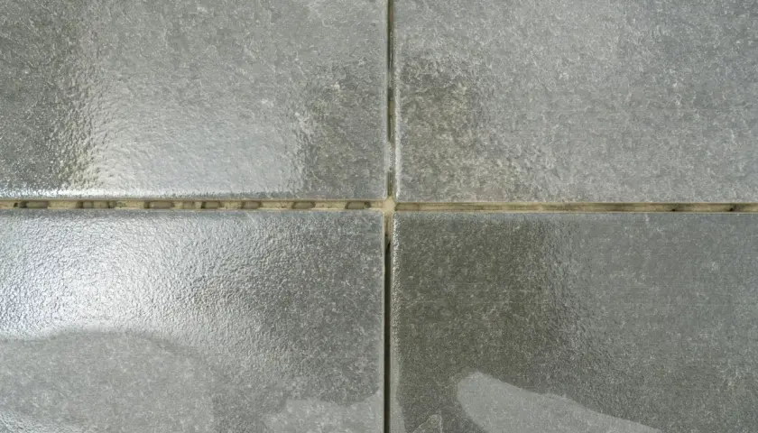 Dettaglio di quattro piastrelle grigie con fughe vuote, pronte per essere riempite. Una guida visiva su come riempire le fughe delle piastrelle.
