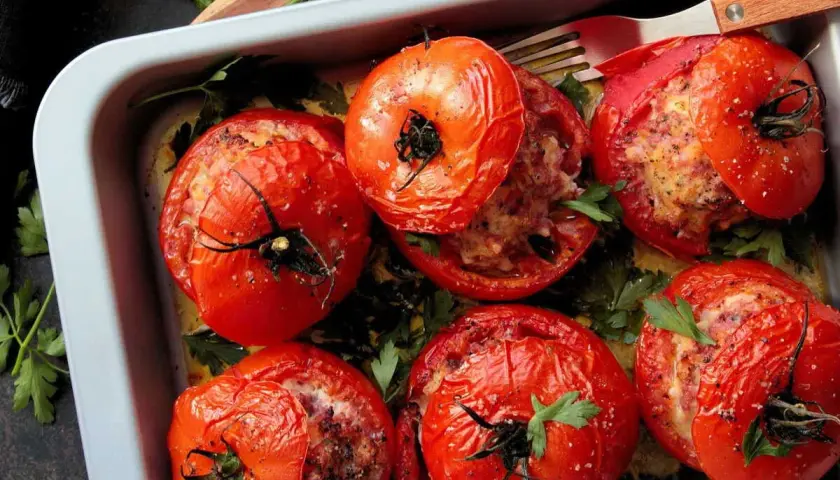 Six tomates farcies dorées, garnies d'une farce savoureuse et parsemées de persil frais, dans un plat de cuisson.