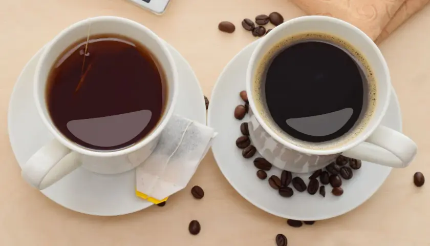 Zwei Tassen, eine mit schwarzem Tee und Teebeutel, die andere mit Kaffee und Kaffeebohnen. Perfekt, um Kaffee und Tee zusammen zu trinken.