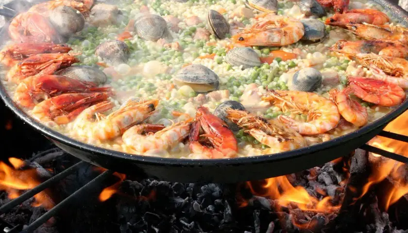 Gros plan sur une paella aux crevettes et palourdes, cuisant sur un feu de bois. Quel vin avec jambalaya ? Un blanc sec ou un rosé fruité serait parfait.