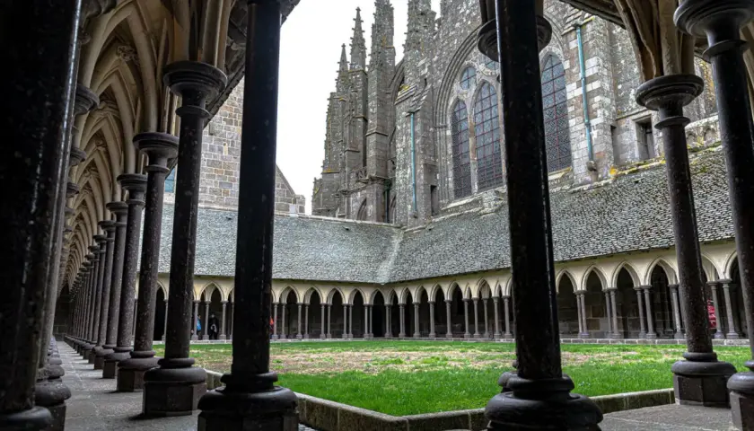 Ein Blick durch die Säulenhalle auf den Kreuzgang des Mont Saint Michel innen. Grüne Wiese und gotische Architektur.