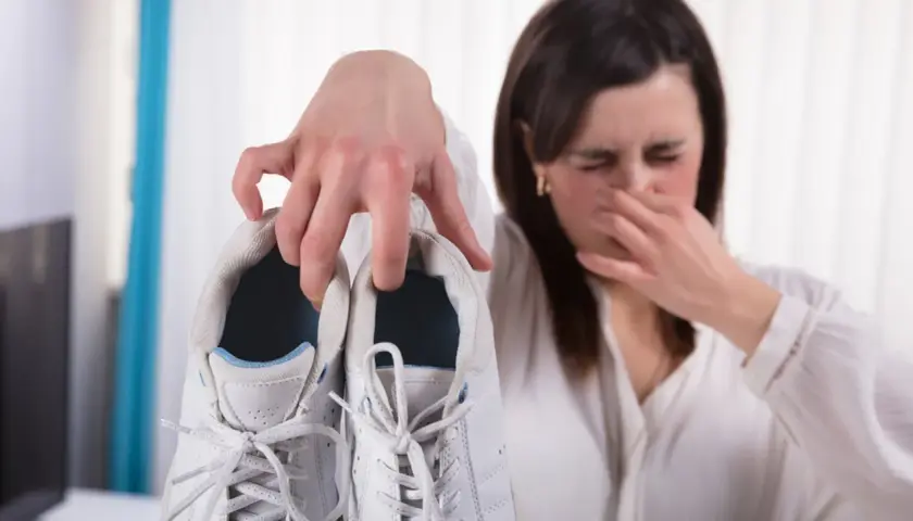 Mujer tapándose la nariz por el fuerte olor de pies que emana de unas zapatillas blancas.