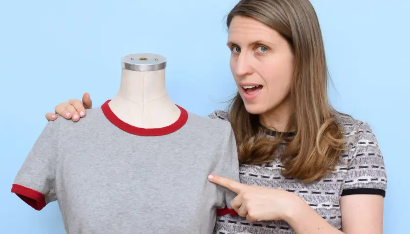 Woman points to a grey t-shirt on a mannequin, demonstrating how to sew a shirt.