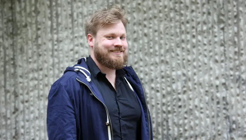 Johannes Klenell ler mot kameran, klädd i en mörkblå jacka över en svart skjorta.