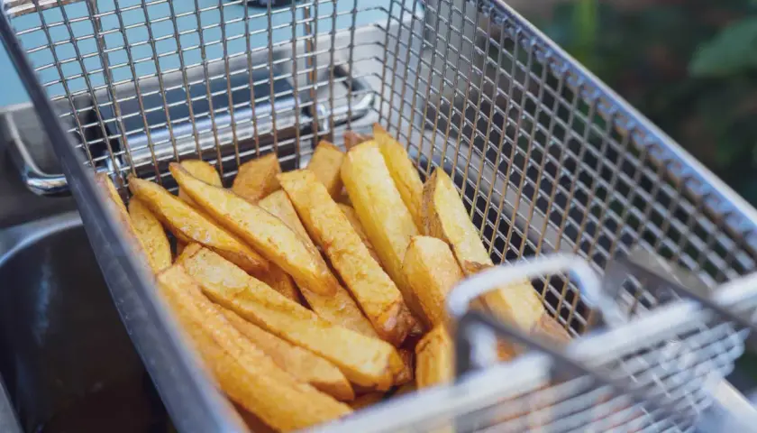 Goldgelbe Pommes in einem Frittierkorb, bereit, um sie wieder knusprig zu machen.