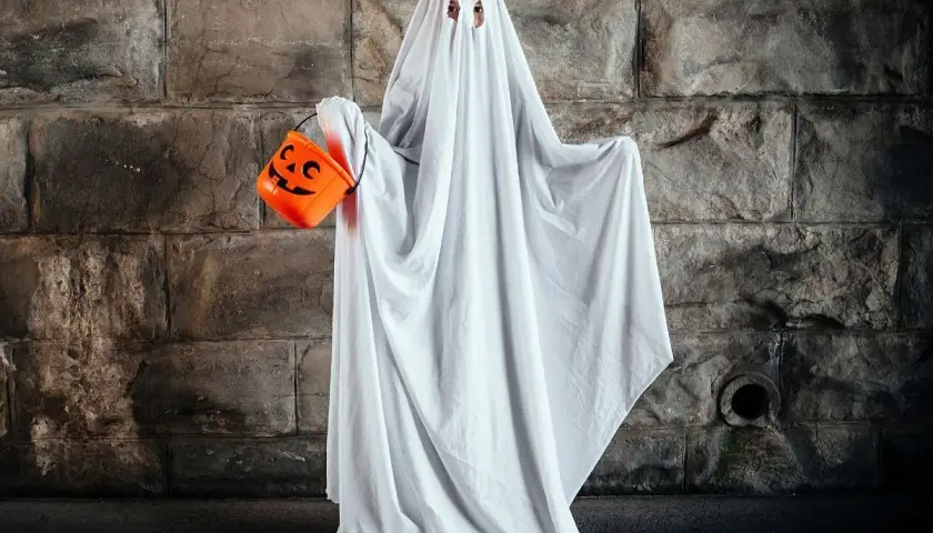 Dziecko w przebraniu na Halloween DIY jako duch, trzymające pomarańczową dynię na cukierki.