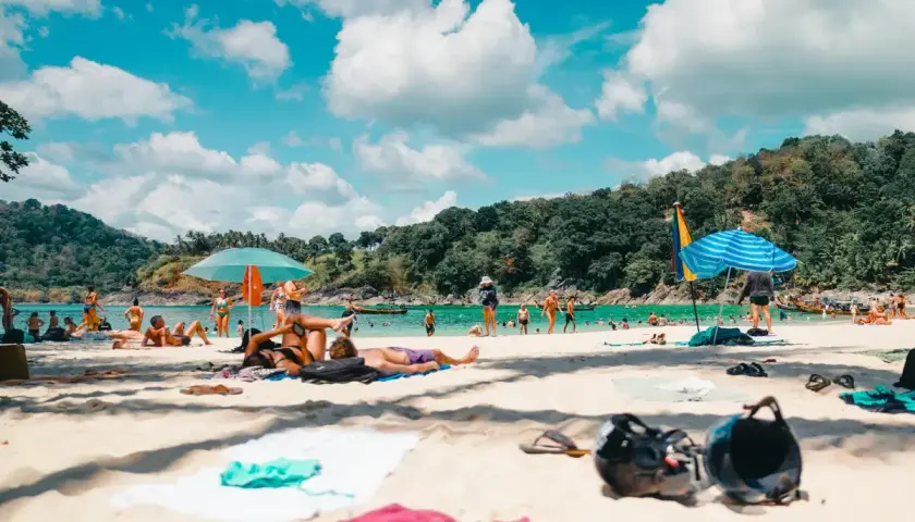 Gente disfrutando de unas **vacaciones agosto 2026** en una playa tropical, con aguas turquesas y vegetación exuberante.