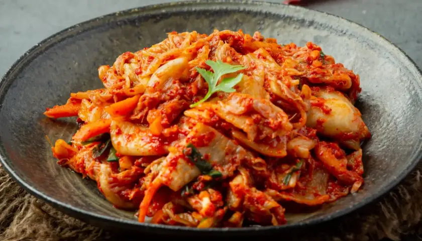 Miseczka z pikantnym kimchi, ozdobiona listkiem kolendry.