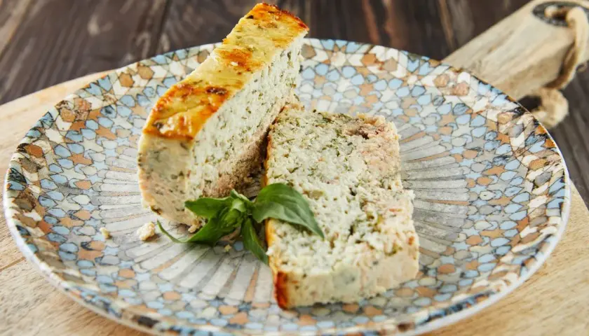 Deux tranches de terrine de poisson aux herbes, garnies d'une feuille de basilic, sur une assiette décorée.