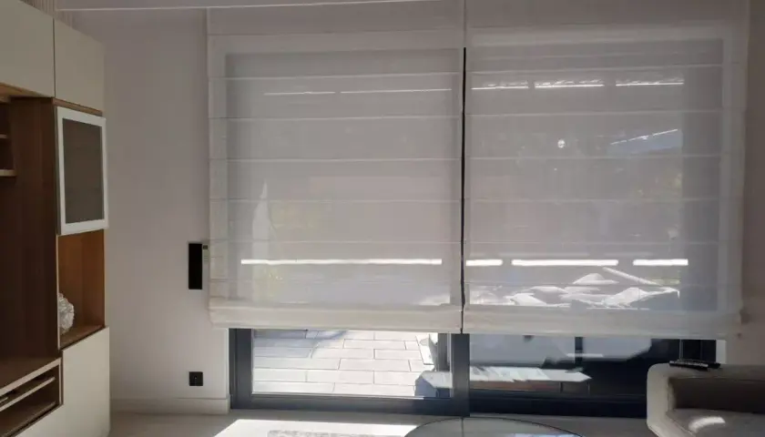 Eleganckie rolety elektryczne wewnętrzne na baterie, wykonane z półprzezroczystego materiału, tworzą przytulną atmosferę w nowoczesnym salonie.