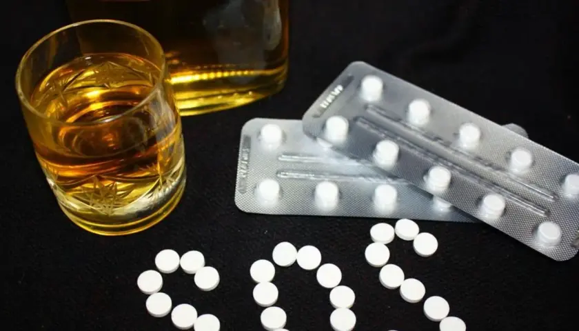 Szklanka alkoholu i blistry z tabletkami, które mogą być benzodiazepiny, ułożone w napis SOS.