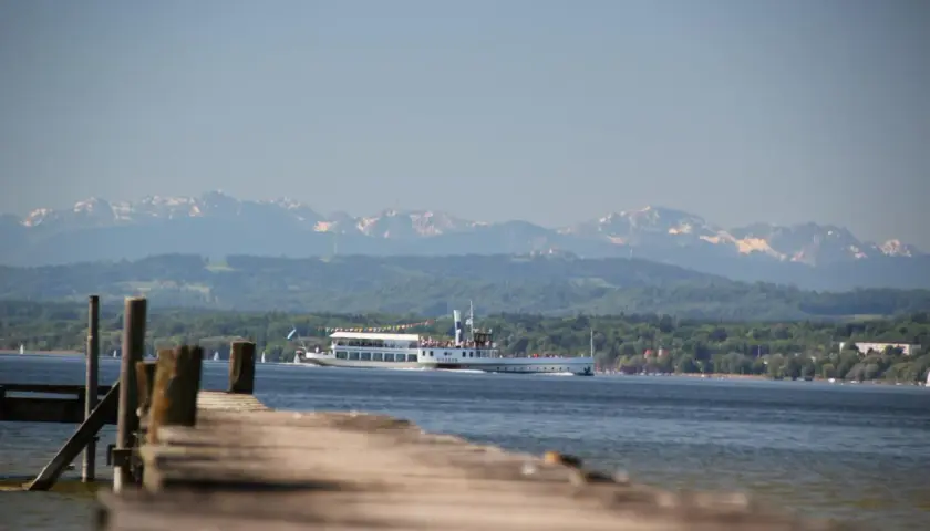 Holzsteg am Ammersee mit einem Ausflugsschiff, im Hintergrund die schneebedeckten Ammersee Berge.