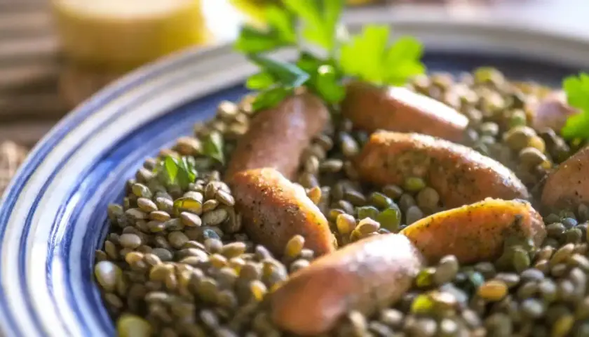 Un plat de lentilles saucisses, garni de persil frais, servi dans une assiette bleue et blanche.