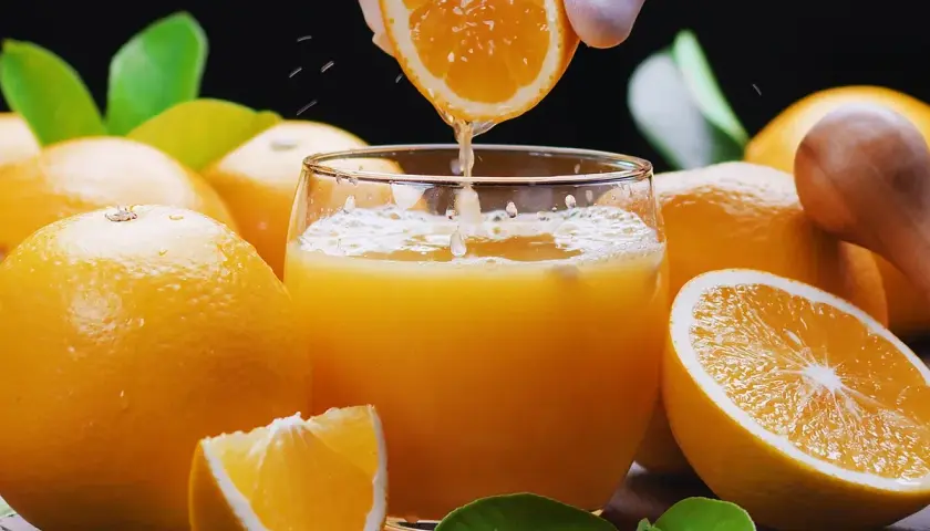 Un vaso de zumo de naranja recién exprimido, rodeado de naranjas frescas. ¡Cuidado! el zumo de naranja engorda si se abusa de él.