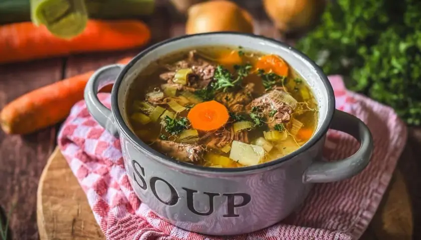 Eine dampfende Schüssel mit Omas frischer Suppe, gefüllt mit zartem Fleisch, Karotten, Sellerie und Kartoffeln.