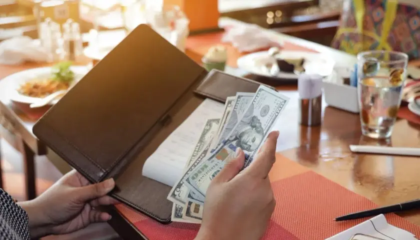 Rachunek w restauracji, ręka trzyma banknoty dolarowe. Poproszę rachunek po angielsku.