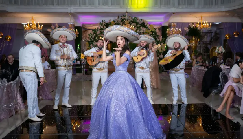 Mariachi grają przyśpiewki weselne, a młoda kobieta w fioletowej sukni posyła całusy.