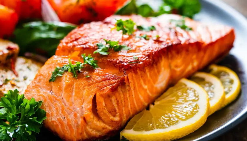 Un succulento filetto di salmone cotto alla perfezione, guarnito con prezzemolo fresco e accompagnato da spicchi di limone e pomodorini.