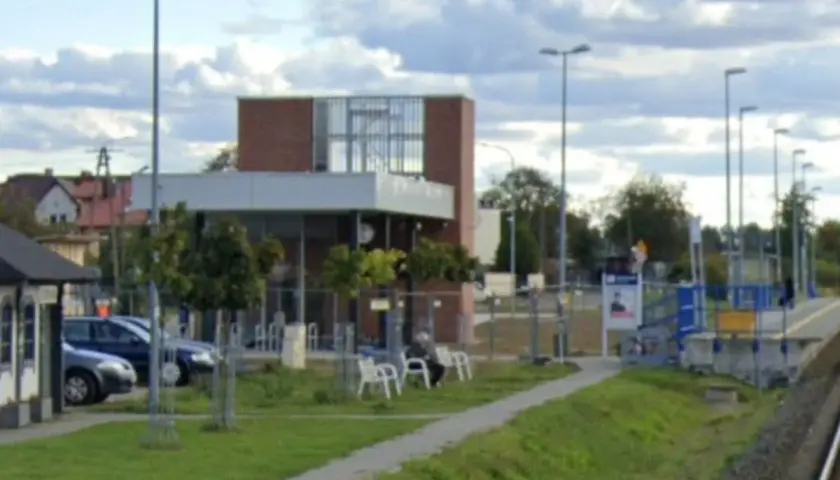Nowoczesna stacja kolejowa z budynkiem, peronem, ławkami i parkingiem.