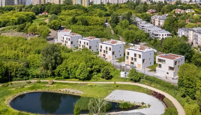 Nowoczesne domy w otoczeniu zieleni, z widokiem na miasto. Widać tu staw i ścieżki spacerowe, idealne do odpoczynku. To miejsce, gdzie życie w stylu sikorskiego vita jest możliwe.