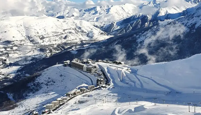 Vista aérea de Saint Lary Soulan, un pueblo de montaña cubierto de nieve con edificios y pistas de esquí, rodeado de majestuosas montañas nevadas.