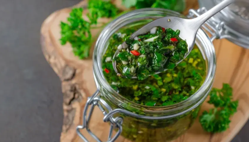Łyżka z aromatycznym chimichurri, pełnym ziół i papryczki, nad słoikiem.