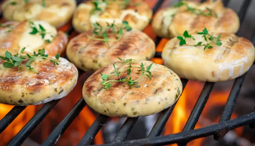 Ronds de halloumi au barbecue, dorés et parsemés de thym frais, grésillant sur les braises ardentes.
