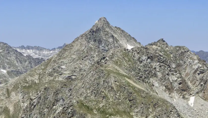 Majestuoso pic de peguera rocoso y escarpado, con nieve en sus cumbres y un cielo azul despejado.