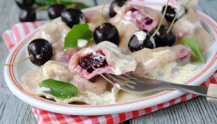 Pyszne pierogi z czereśniami, polane śmietaną, ozdobione świeżymi owocami i listkami mięty. Idealne na letni deser.