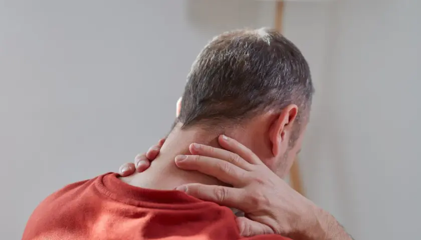 Mężczyzna masuje kark, szukając ulgi w bólu. Rozważa wdowi garb ćwiczenia w domu, by poprawić postawę.