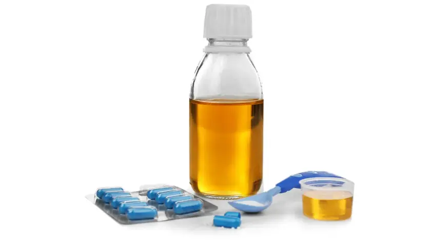 Flacone di sciroppo amoxicillina bambini, blister di capsule blu e misurino dosatore con polvere bianca.
