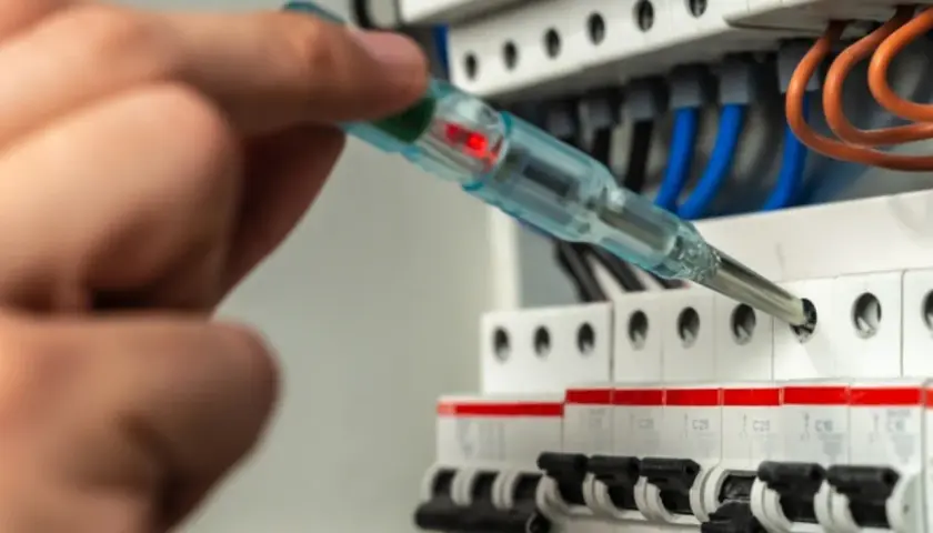 Dłoń z próbnikiem napięcia przy bezpiecznikach elektrycznych.