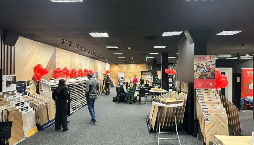 Wnętrze salonu z wystawionymi panelami podłogowymi, dekoracjami z balonów i ludźmi.