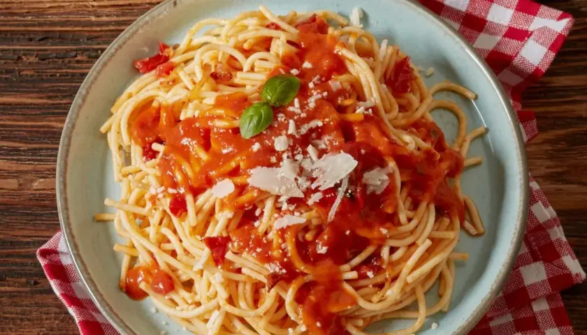 Spaghetti z sosem pomidorowym, parmezanem i bazylią na talerzu.