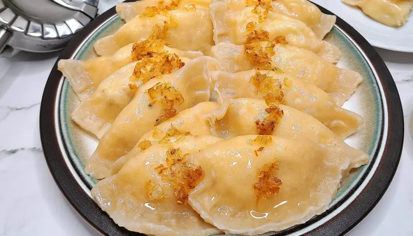Talerz pełen pysznych pierogów ruskich, polanych tłuszczem i posypanych skwarkami. Idealne, by pokazać, jak zrobić pierogi ruskie.