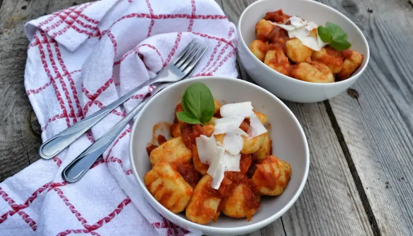 Dwa talerze pysznych gnocchi z sosem pomidorowym, posypane parmezanem i udekorowane bazylią, gotowe do podania.